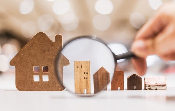 Hand holding magnifying glass and looking at house model, house selection, real estate concept.